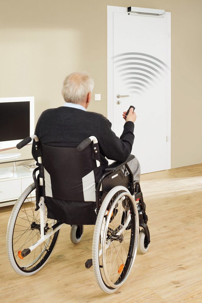 Rollstuhlfahrer bedient mittels Handsender einen Antrieb zur Öffnung einer Innentür